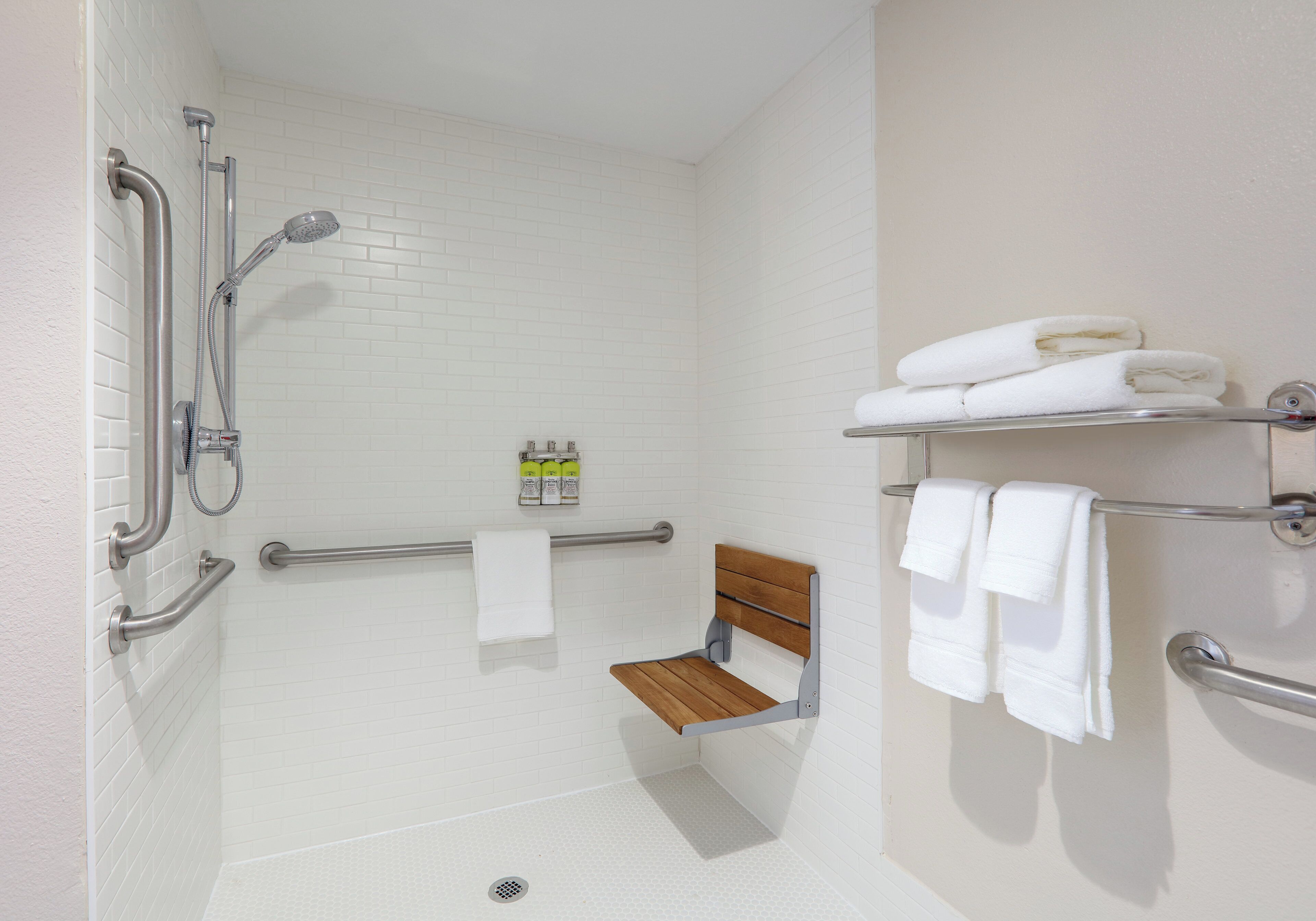 A bathroom with a shower, grab bars, a bench, and towel racks.