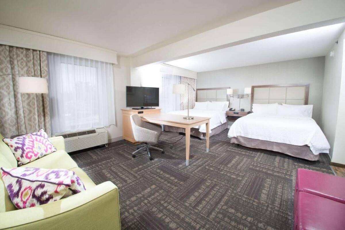 A hotel room with a bed, a desk, a chair, a television, and a window with curtains.