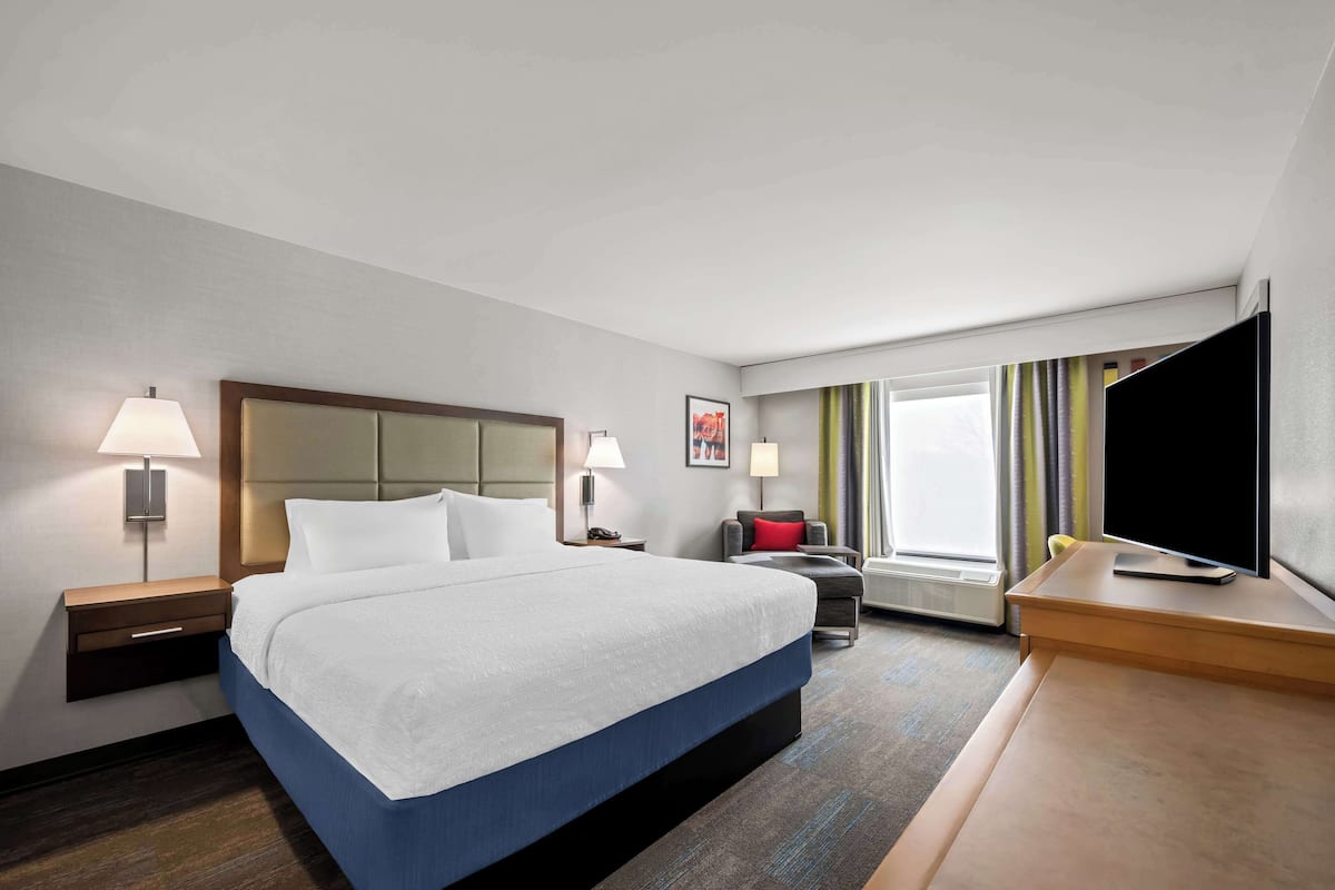 A hotel room with a large bed, bedside tables with lamps, a desk with a TV, and a window with curtains.