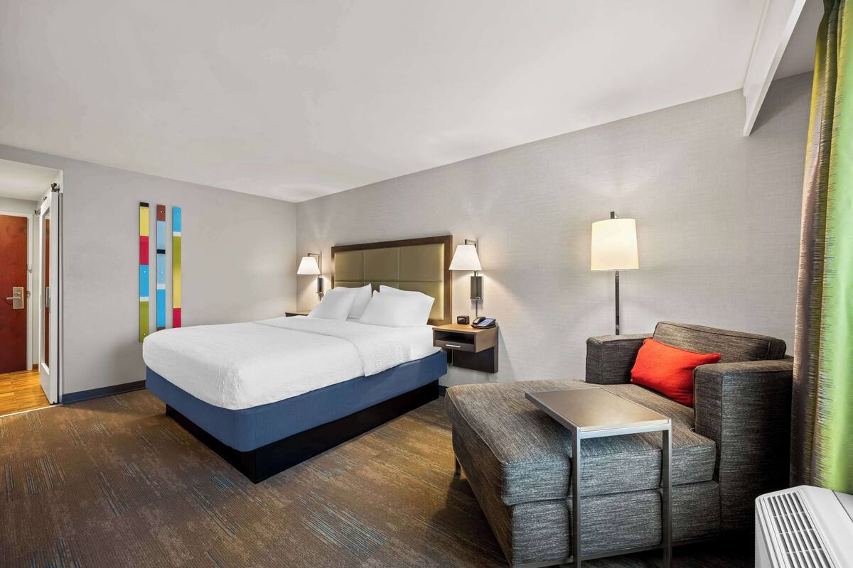 A hotel room with a bed, bedside tables, a chair, and a small table.