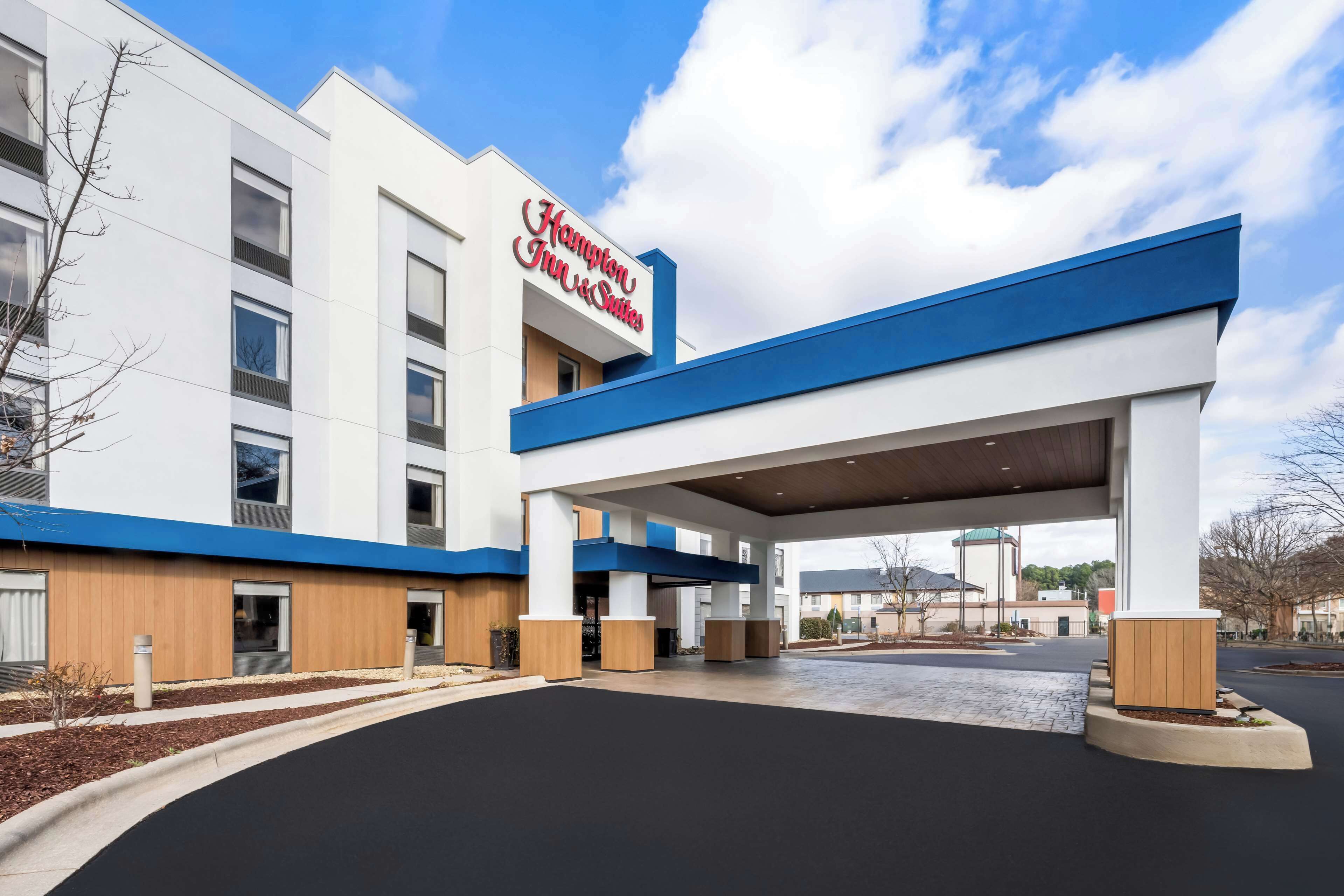 A Hampton Inn & Suites hotel with a modern facade, large entrance canopy, and a clear sky.