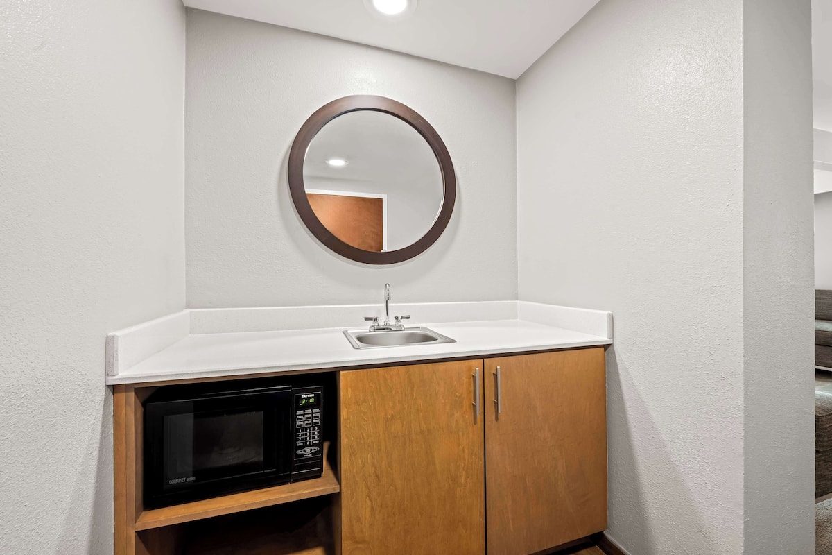 A compact kitchenette with a microwave, sink, and wooden cabinets.