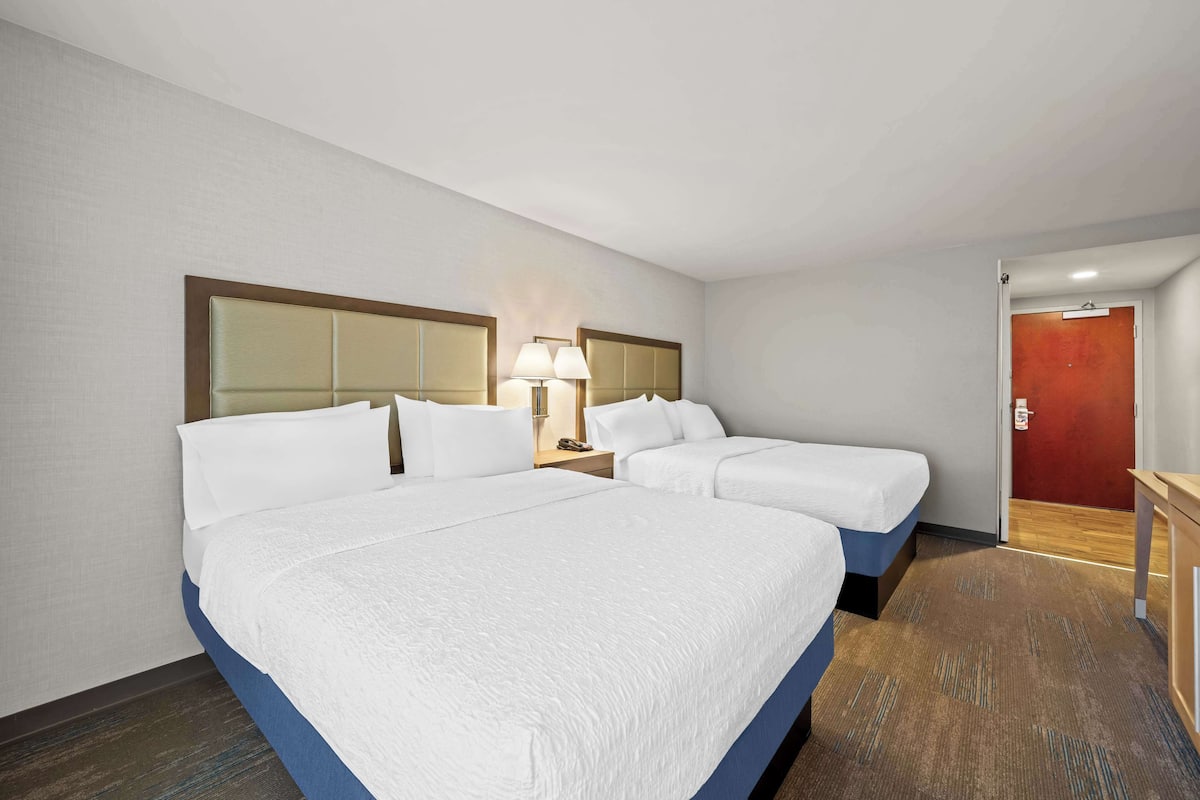 A hotel room with two beds, a nightstand with a lamp, and a red door.