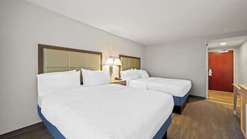 A hotel room with two beds, a nightstand with a lamp, and a red door.