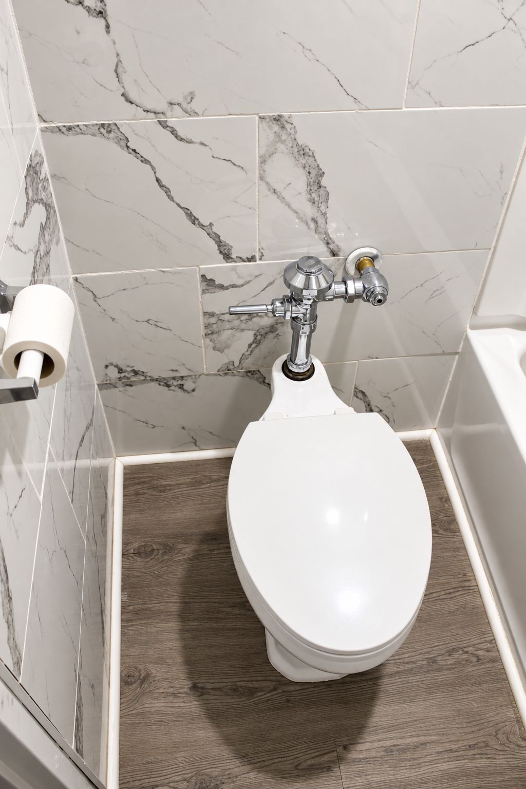 A toilet with a marble-tiled wall and a wooden floor.