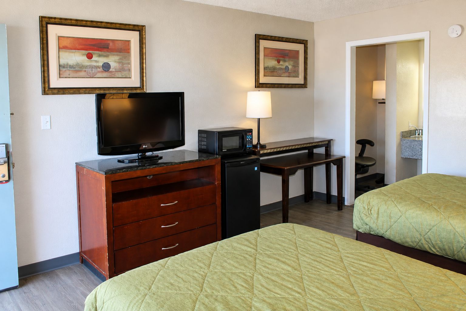 A hotel room with a TV, microwave, desk, two beds, and artwork on the wall.