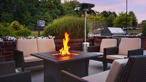 An outdoor seating area with a fire feature, wicker chairs, and a grill in the background. - Residence Inn by Marriott Poughkeepsie (Poughkeepsie)