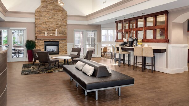 A spacious living area with a stone fireplace, comfortable seating, a kitchen with bar seating, and large windows. - Residence Inn by Marriott Poughkeepsie (Poughkeepsie)