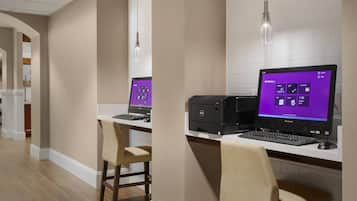 A modern hotel room with a desk, two computers, and a chair.