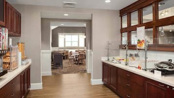 A modern kitchen with wooden cabinets, a breakfast bar, and a dining area with a carpeted floor.
