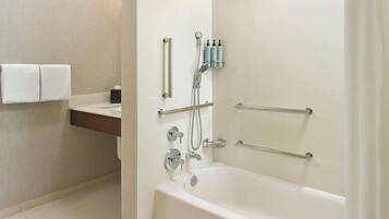 A modern bathroom with a bathtub, shower, and handrails.