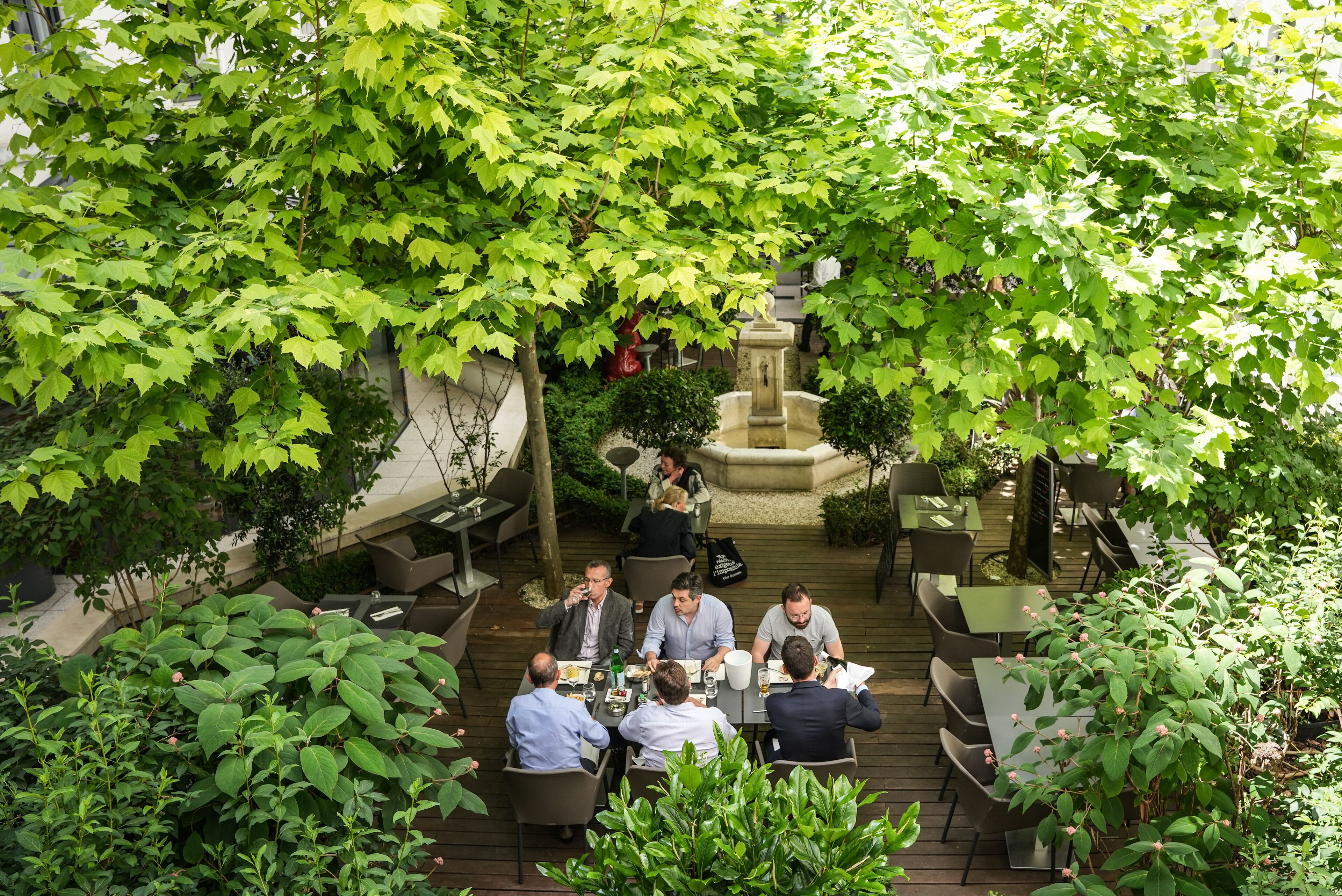 A group of people dining outdoors at a restaurant with a fountain and lush greenery.