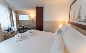 Habitaci ón de hotel con una cama, dos toallas, un escritorio con sillas, un letrero en la pared y un cuadro con la Torre Eiffel.