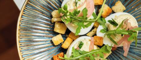 Une assiette d’œufs mimosa décorée de roquette et de lardons, présentée sur une assiette aux motifs bleus et dorés.