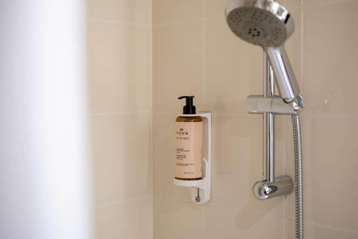 A shower with a handheld showerhead and a bottle of body wash on a wall-mounted holder.