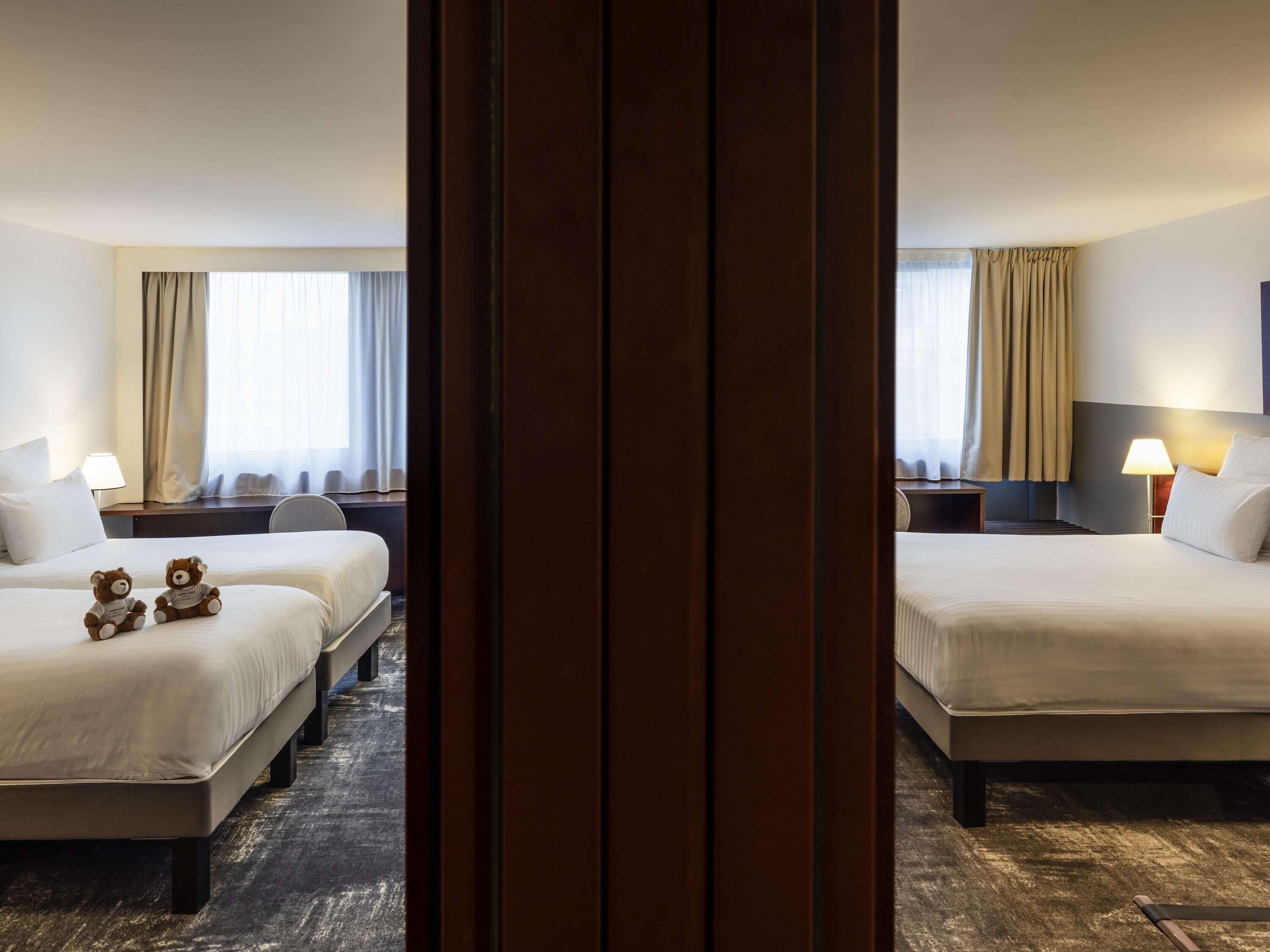 Een hotelkamer met twee bedden, een bureau, een stoel, een lamp en twee teddyberen op het bed.