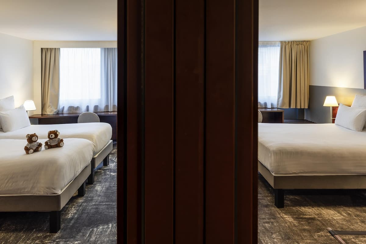 A hotel room with two beds, a desk, a chair, a lamp, and two teddy bears on the bed.