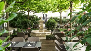 An outdoor dining area with tables and chairs, a central fountain, and lush greenery. - Mercure Paris Gare Montparnasse TGV (Paris)