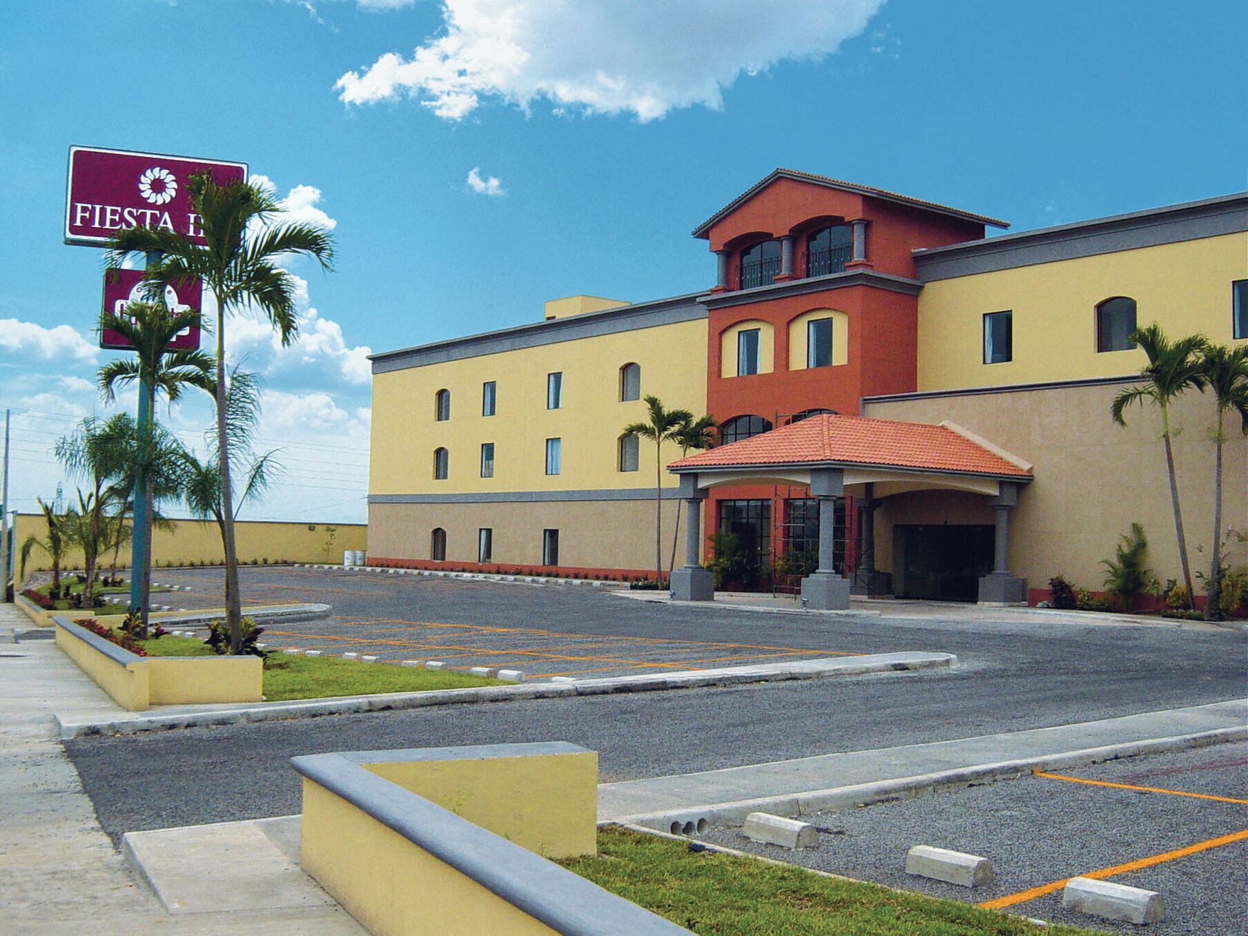 A hotel with a yellow facade, a red roof, and a sign reading "Fiesta Inn."