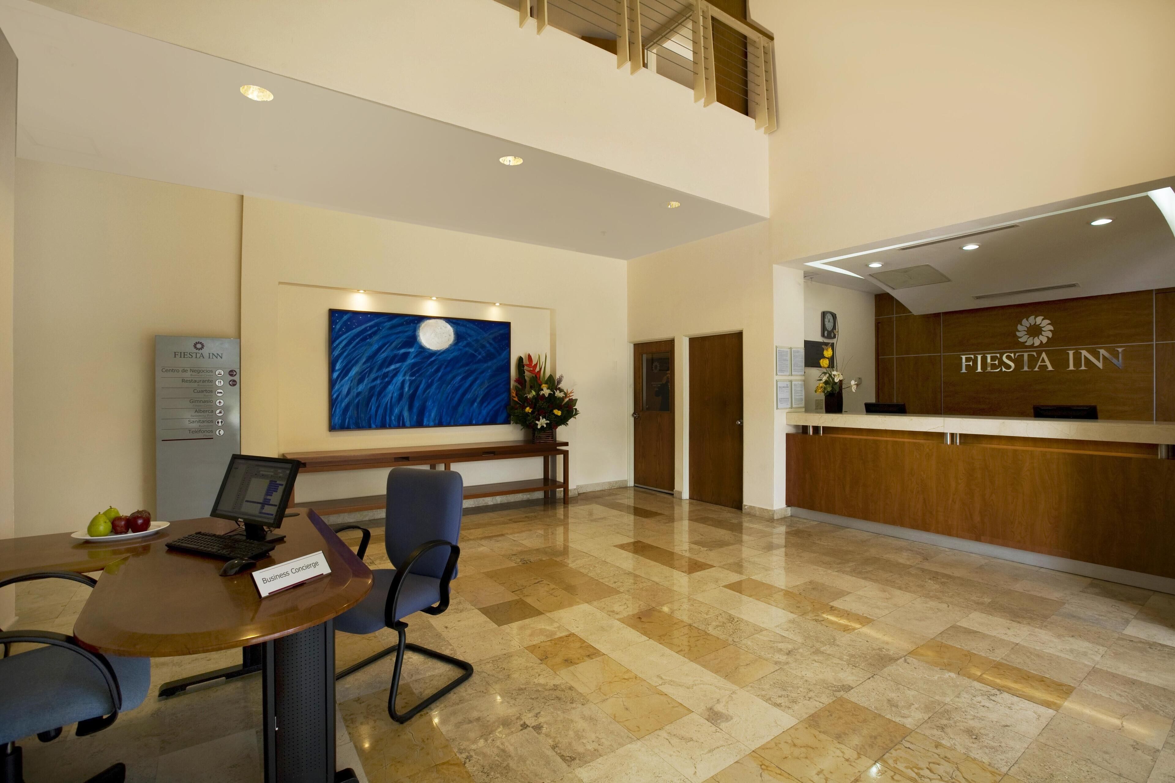 A hotel reception area with a desk, chairs, a computer, and a painting of a night sky.