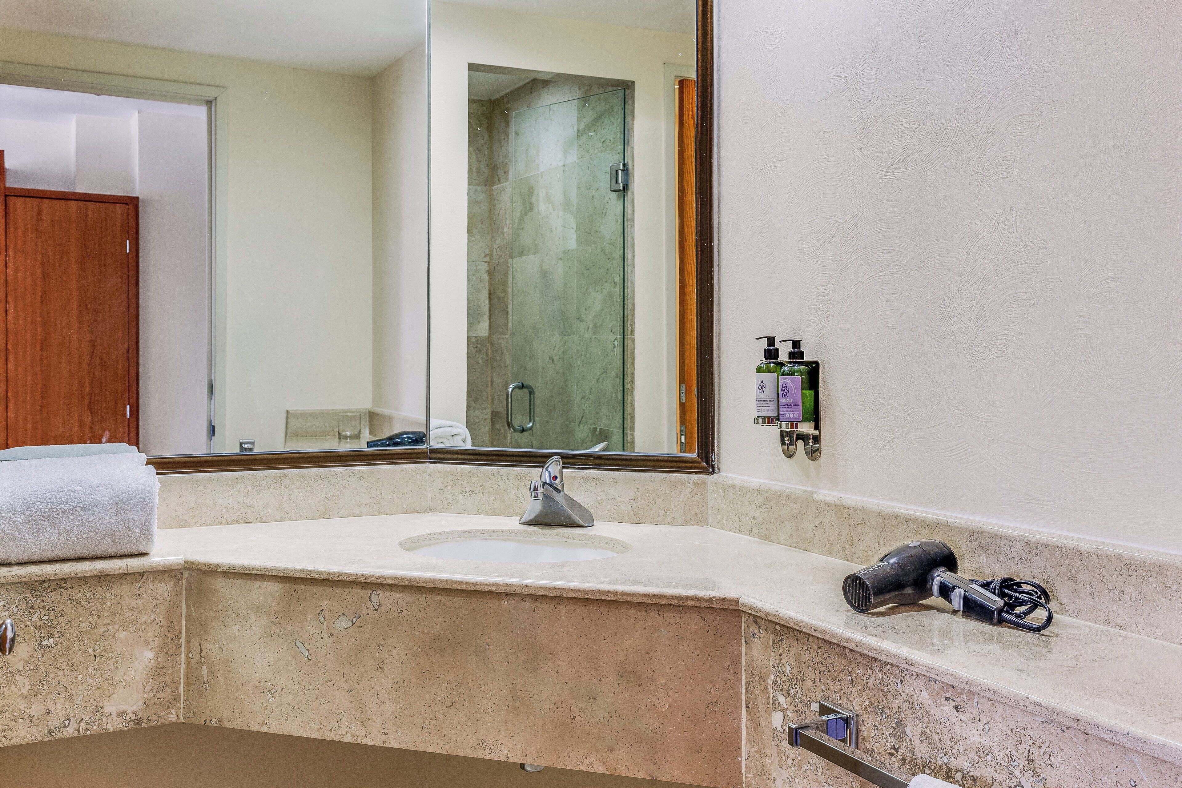 Un baño con lavamanos de mármol, un espejo grande, una toalla en la encimera y un secador de pelo.