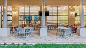 An outdoor dining area with tables and chairs, large windows, and columns. - Fiesta Inn Colima (Colima)