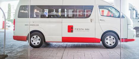 Una camioneta blanca con detalles rojos estacionada frente a la entrada de un hotel.