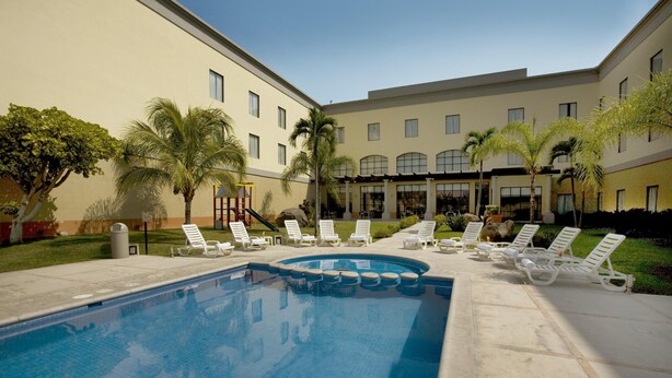 A swimming pool with lounge chairs and palm trees. - Fiesta Inn Colima (Colima)