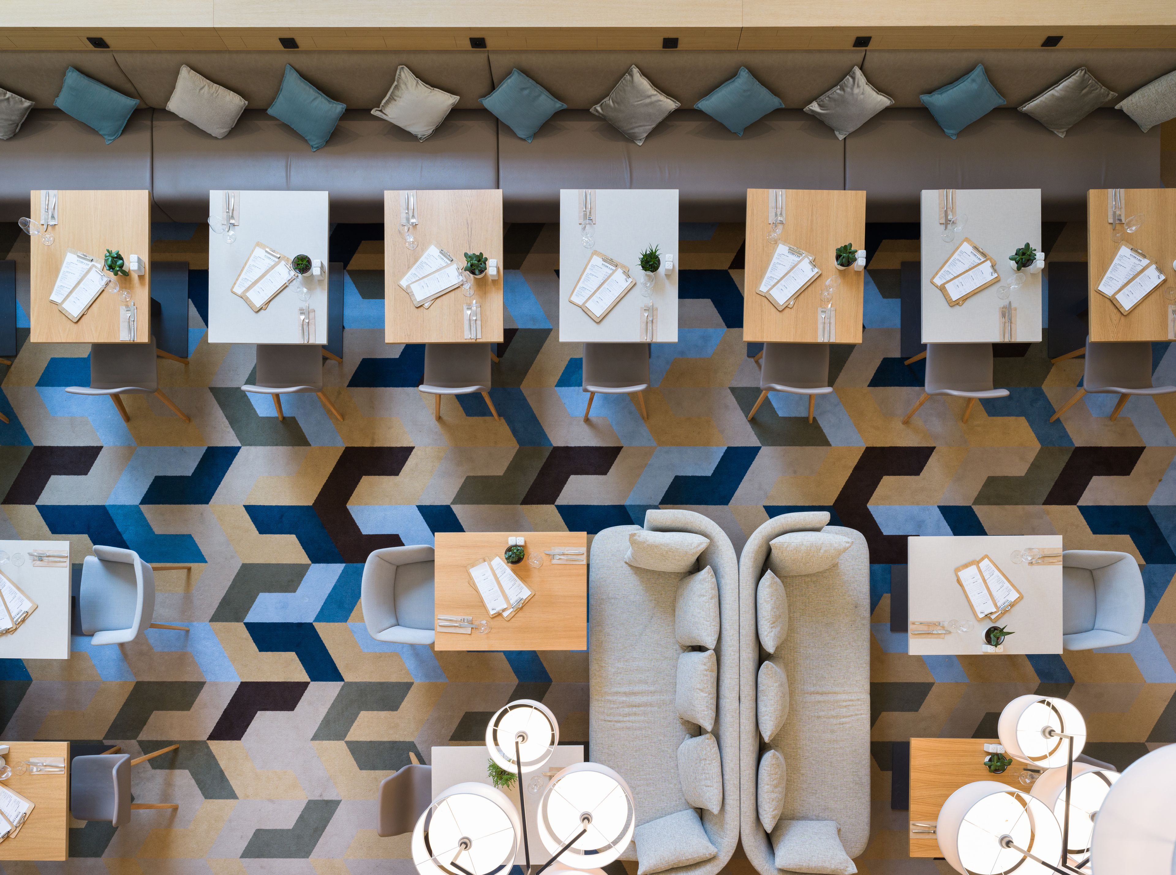 A modern hotel lobby with multiple seating areas, including sofas and tables, arranged in a geometric pattern.