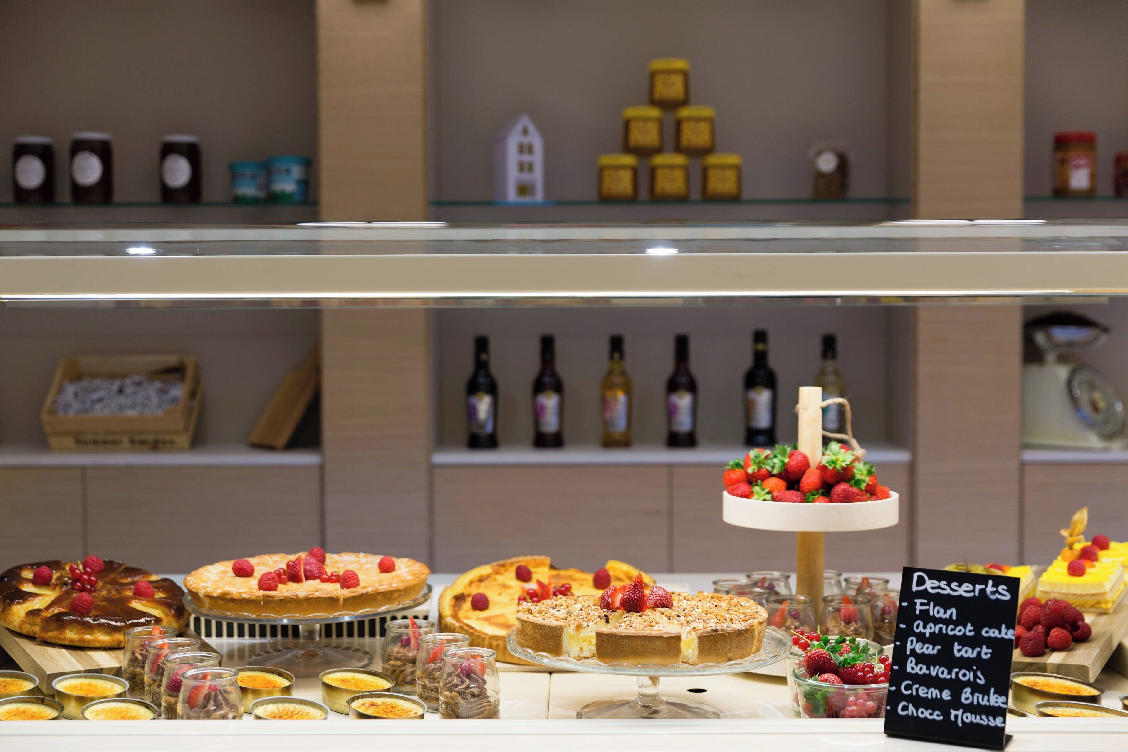 A dessert display with various cakes and pastries, including a flan, apricot cake, pear tart, Bavarois, and Choco Mousse.