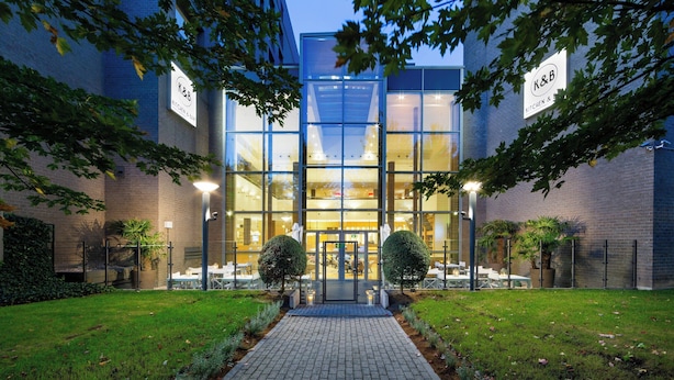 A modern building with a glass facade, labeled "K&B Kitchen & Bar," featuring a paved entrance and well-maintained landscaping. - Courtyard by Marriott Brussels (Brussels)