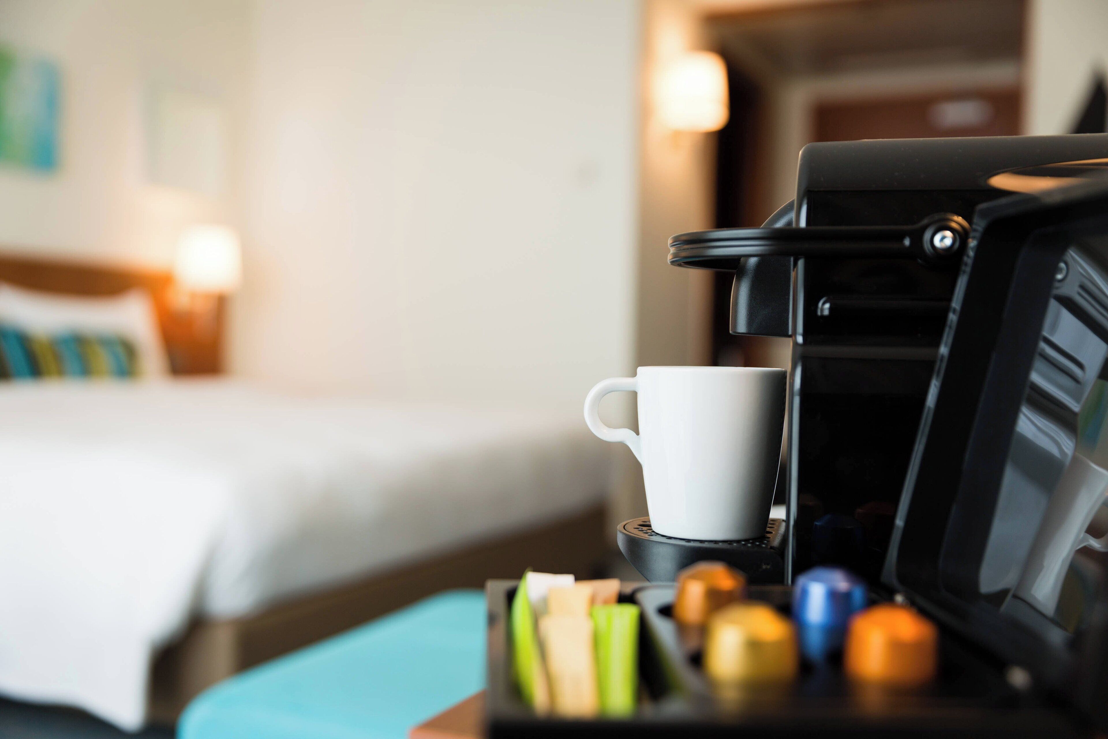 Una màquina de cafè amb una tassa i un safata de càpsules de cafè a una habitació d'hotel.