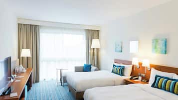 Une chambre d’hôtel avec deux lits, un bureau avec une télévision, une lampe et une fenêtre avec des rideaux.
