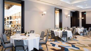 A hotel dining area with round tables, chairs, and a patterned carpet.