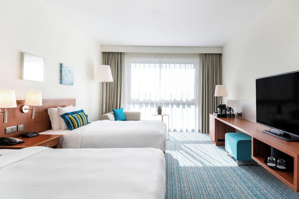 Ein Hotelzimmer mit zwei Betten, einem Fernseher, einem Schreibtisch und einem Fenster mit Vorhängen.