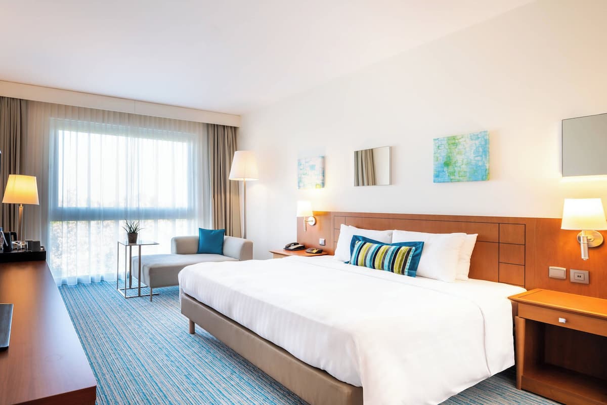 Ein Hotelzimmer mit einem großen Bett, einem Schreibtisch, einem Stuhl und einem kleinen Tisch mit einer Pflanze.