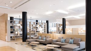 A modern library with a sectional sofa, round tables, and bookshelves. - Courtyard by Marriott Brussels (Brussels)