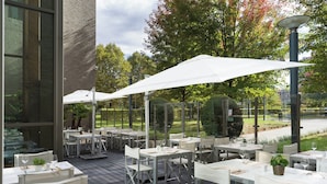 An outdoor dining area with tables and chairs, umbrellas, and potted plants. - Courtyard by Marriott Brussels (Brussels)