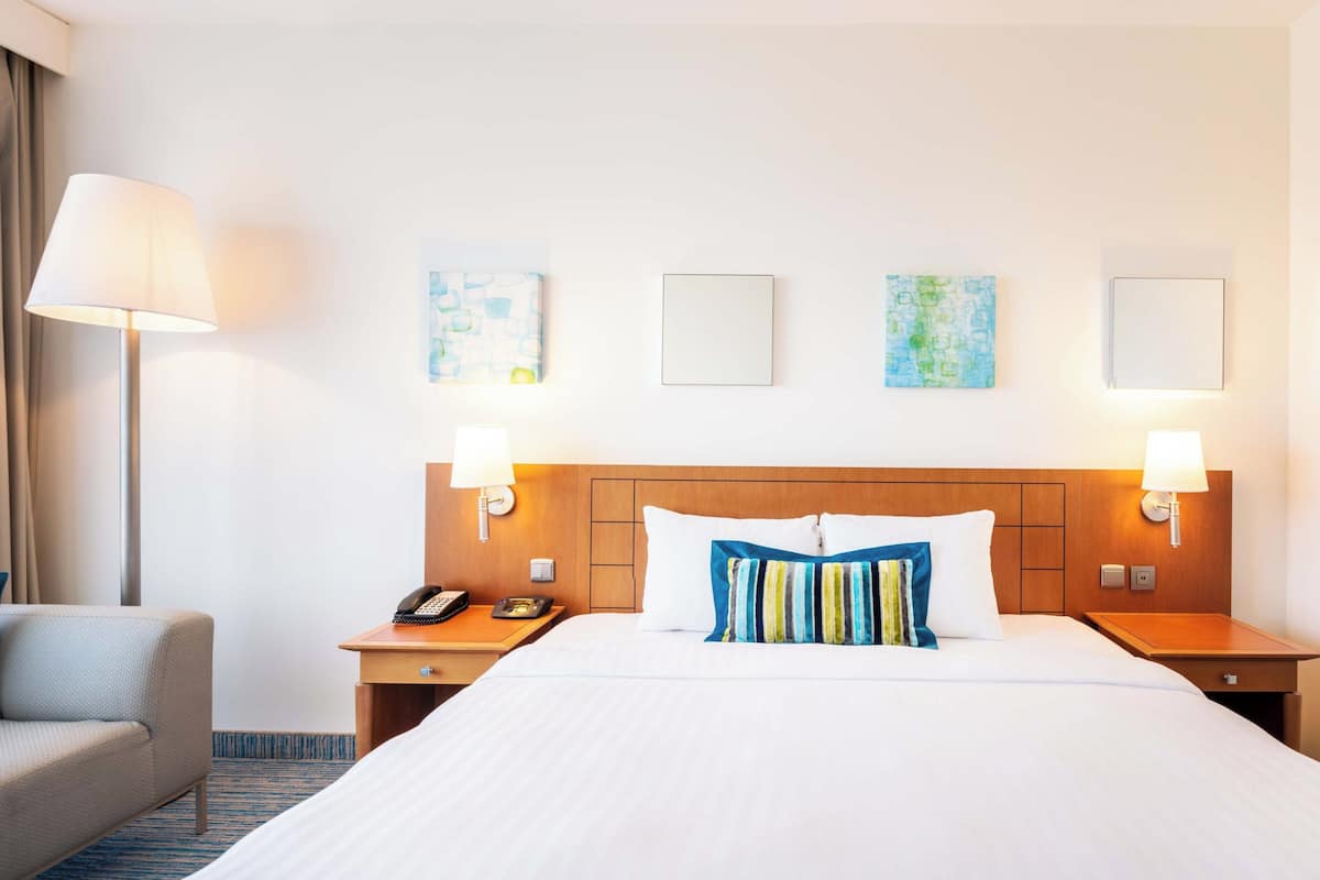Ein Hotelzimmer mit einem großen Bett, zwei Nachttischen, einer Lampe und einem Kunstwerk an der Wand.