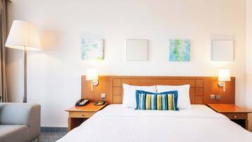 Habitación de hotel con una cama grande, dos mesitas de noche, una lámpara y una obra de arte en la pared.