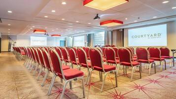 Ein Konferenzraum mit Reihen roter Stühle, Teppichboden und einer großen Leinwand, die "COURTYARD BY MARRIOTT" zeigt.