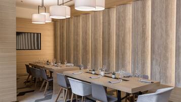 A modern conference room with a long table set for dining, grey chairs, and pendant lighting.