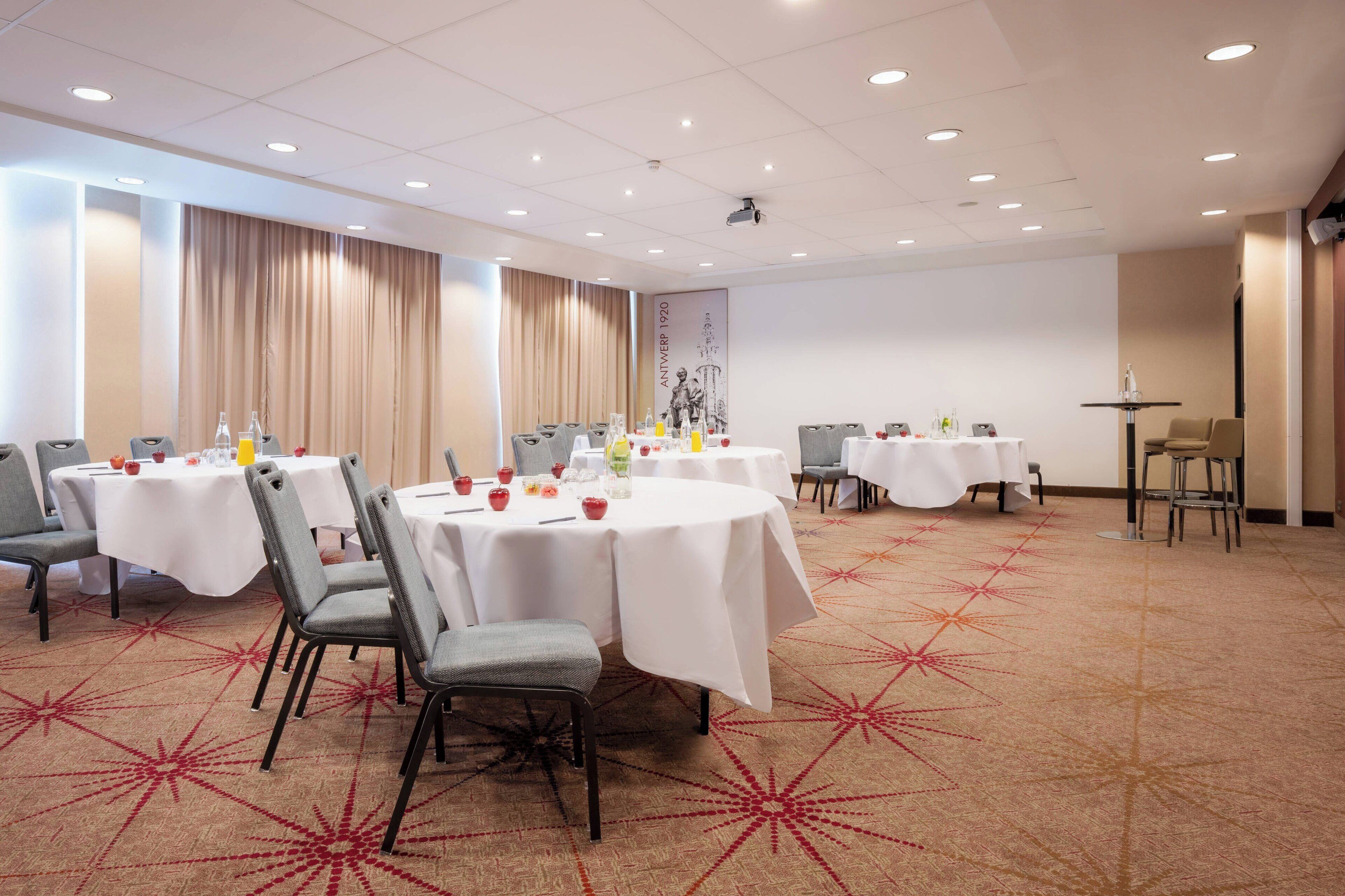 A conference room with round tables, chairs, and a carpeted floor.