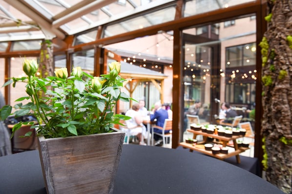 A wooden planter with green plants on a table in a restaurant with outdoor seating.