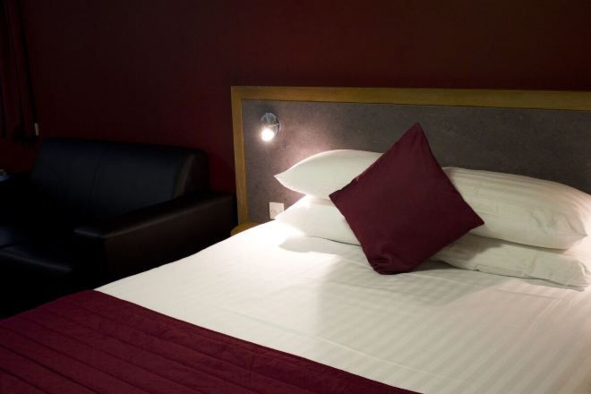 Habitació d'hotel amb llit, tauleta de nit i cadira.