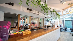 Un moderno bar con mostrador de madera, estantes llenos de botellas y plantas colgantes.