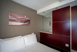 Habitación de hotel con cama, un cuadro grande en la pared, un espejo y un armario rojo.