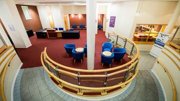 A hotel lobby with a red carpet, blue chairs, a reception desk, and a staircase.