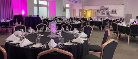 A banquet hall with round tables set for dining, chairs, and a large decorative centerpiece.