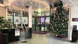 Zona de recepción de un hotel con un árbol de Navidad, un mostrador de recepción y un cartel que indica la disponibilidad de habitaciones.
